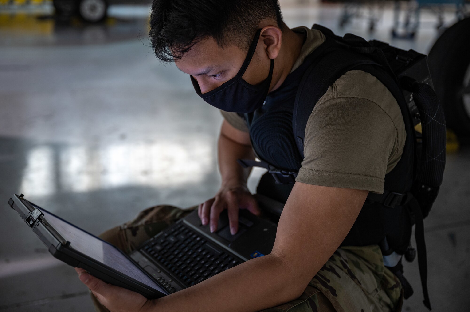 An Airman works on a laptop while under an F-22 Raptor.