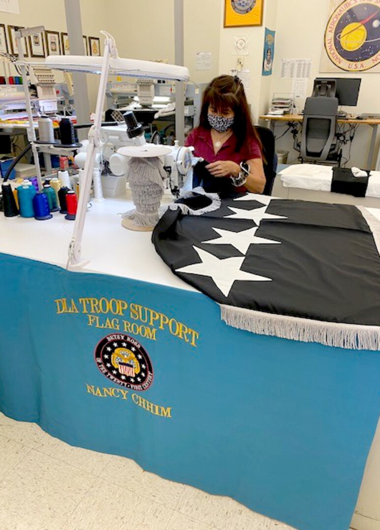 DLA Troop Support sewing machine operator Nancy Chhim applies silver fringe to a flag in the Clothing and Textiles flag room in Philadelphia, July 29, 2020. Chhim is one of three flag room employees who’ve proven essential to the flag room’s mission since the COVID-19 pandemic began in March.