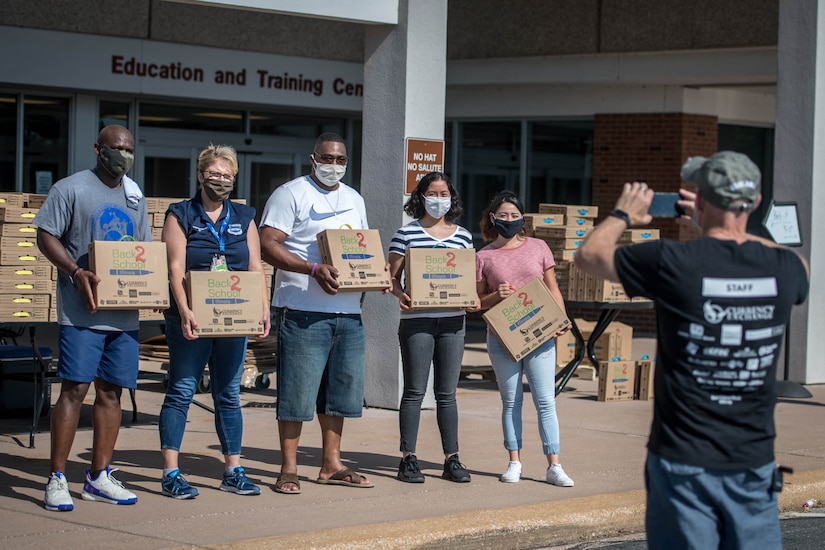 Five people, holding boxes, stand in front of the education center for a group photo.