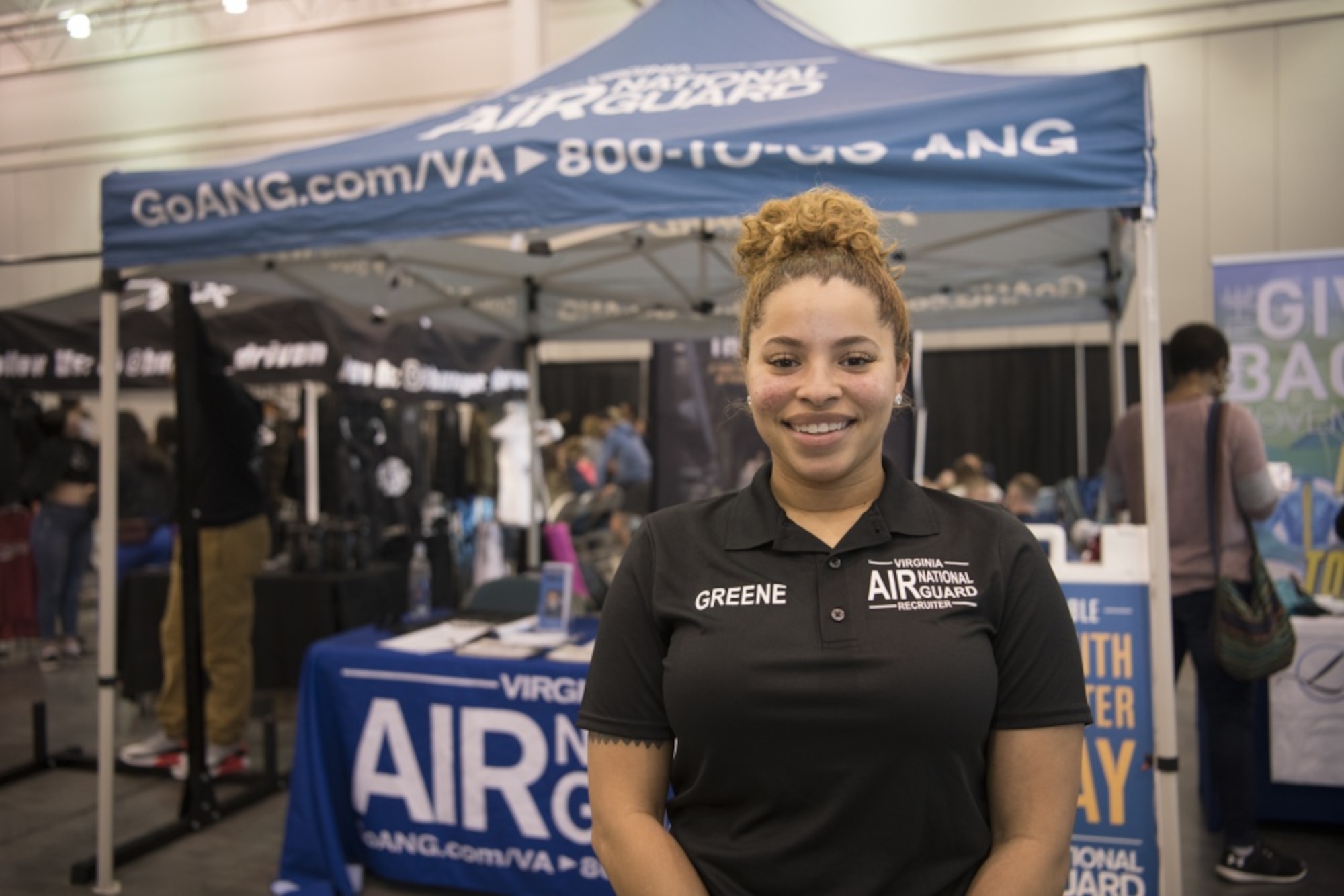An Air National Guard recruiter is smiling in front of her tent at an event