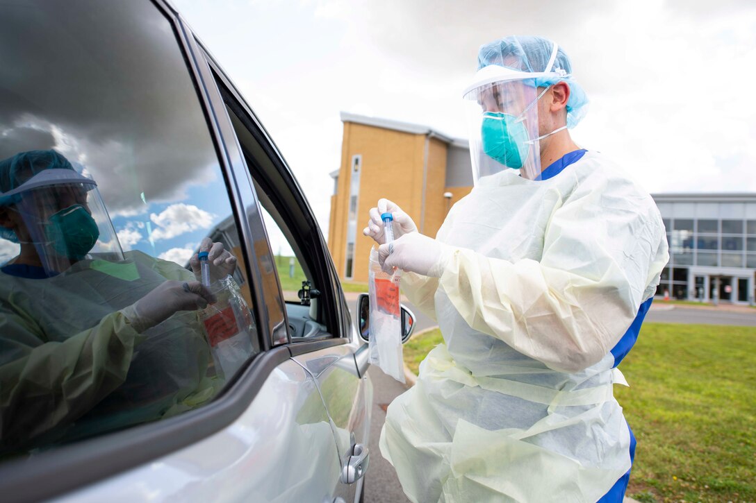 An airman wearing personal protective stands outside of a car.