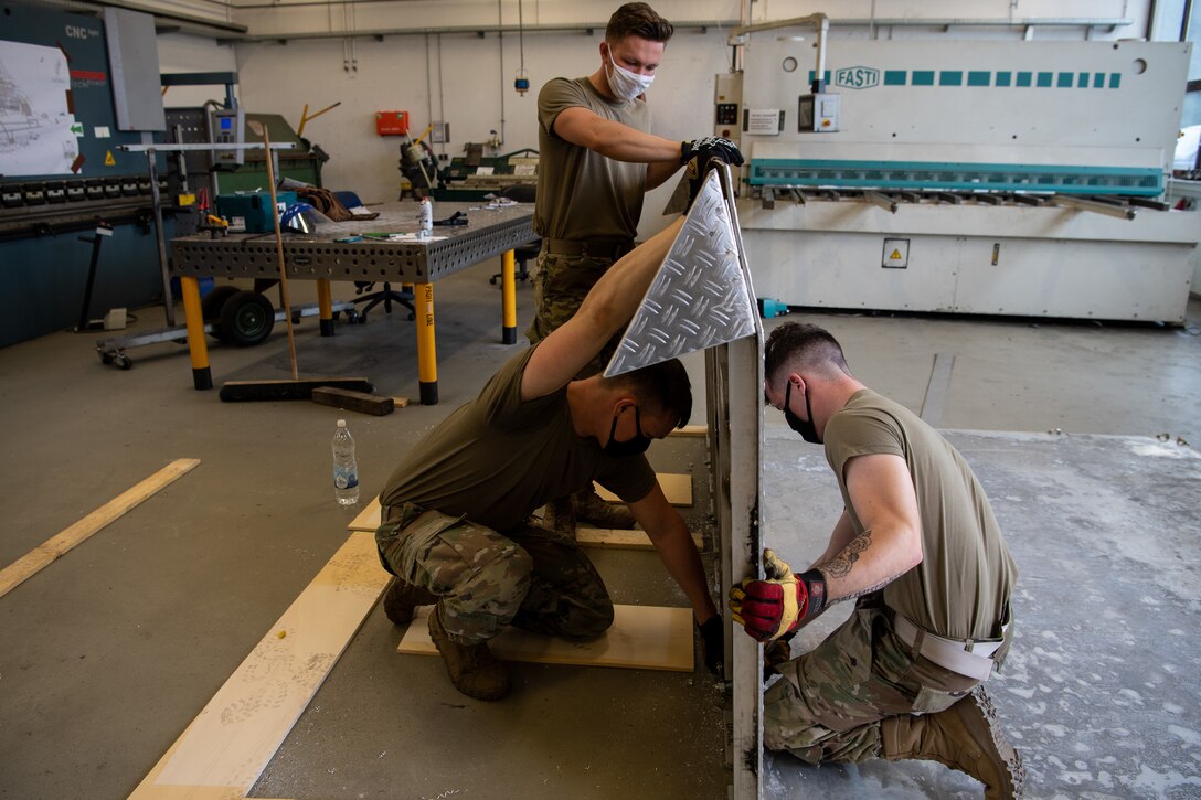 U.S. Air Force Airman 1st Class Tyler Sellitto, middle, Senior Airman Dyllan Greer, left, and Airman 1st Class Austen Campbell, structural journeymen from the 786th Civil Engineer Squadron, assemble a bio containment unit ramp at Ramstein Air Base, Germany, Aug. 10, 2020.