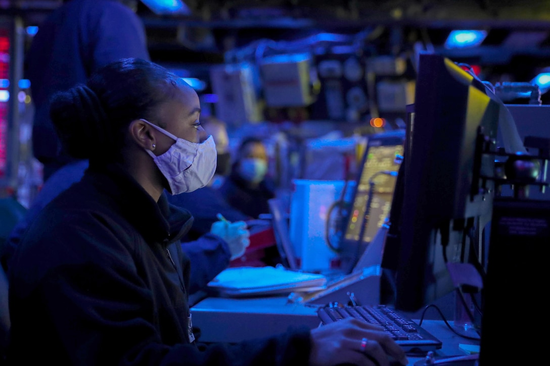 A sailor stares at a computer screen in a dimly lit room.