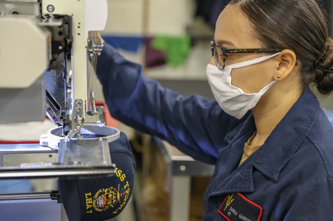 An airman uses a machine to embroider a ball cap.