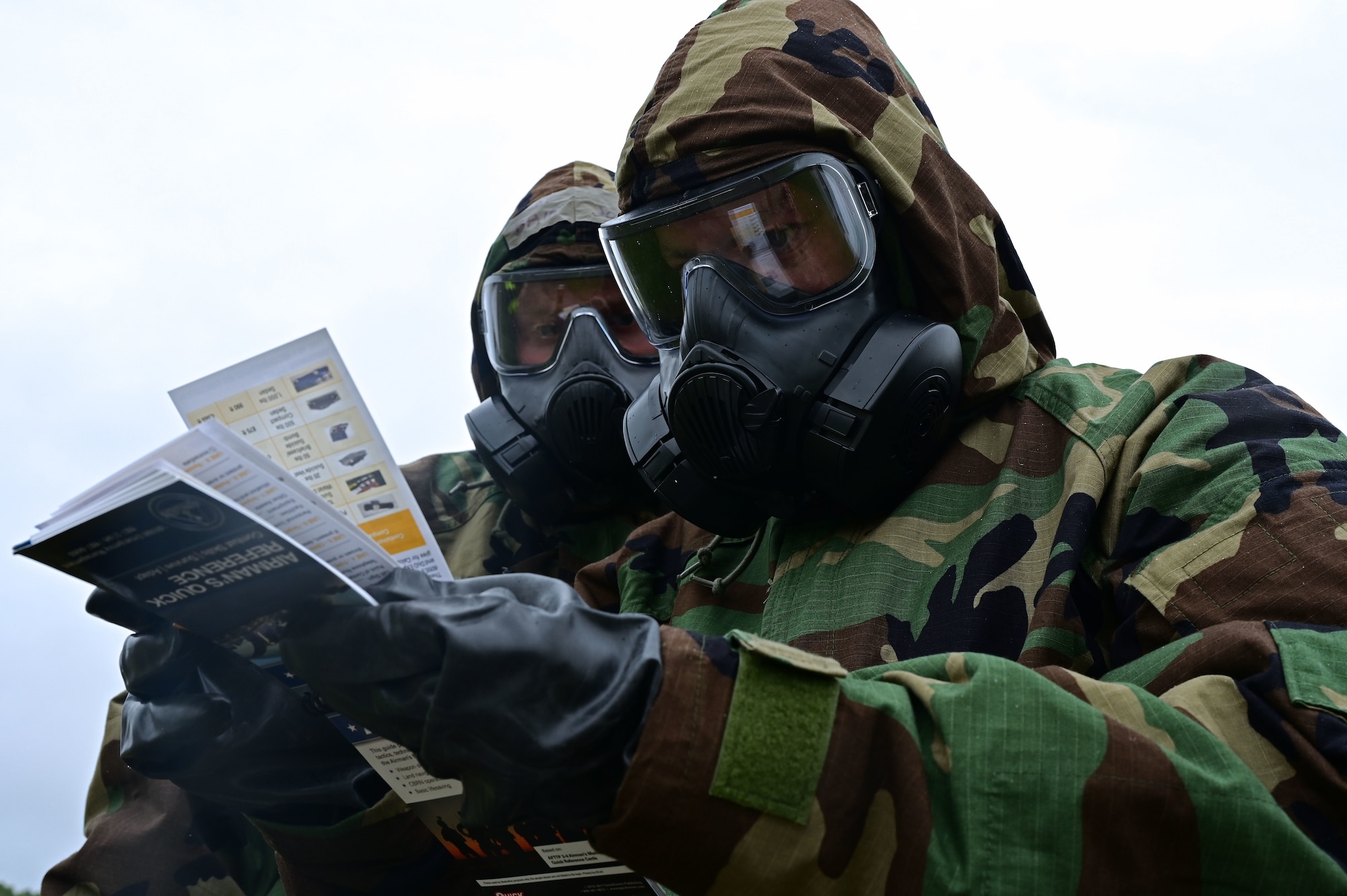 Airmen in mopp gear read an Airman's Quick Reference Guide.