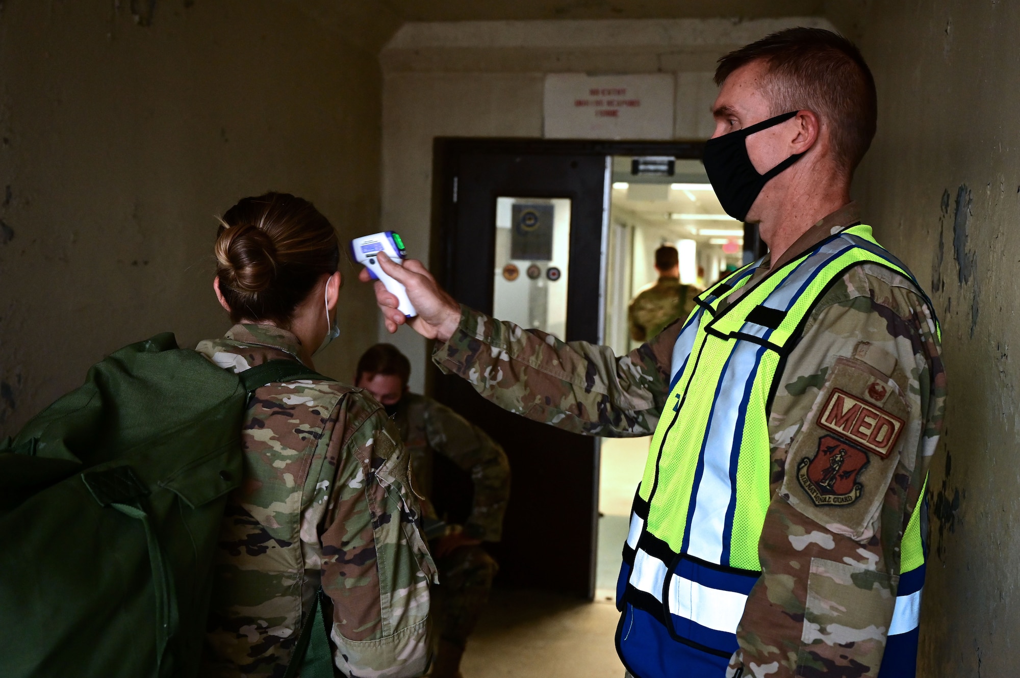 An Airman checks the temperature of other Airmen before entering a building.