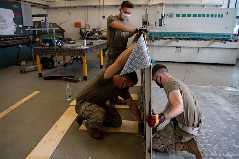 Airmen wearing face masks assemble a ramp.