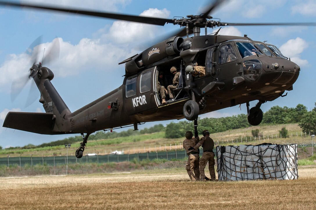 Soldiers stand underneath a helicopter.