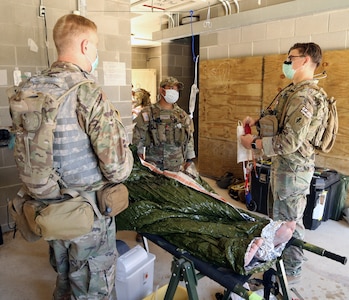 Three Soldiers work on a simulated patient in a building.