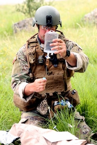 Soldier/medic works with an IV bag in the field.