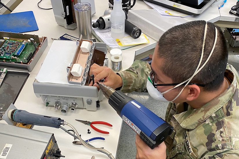 A man wearing a face mask repairs a ventilator.