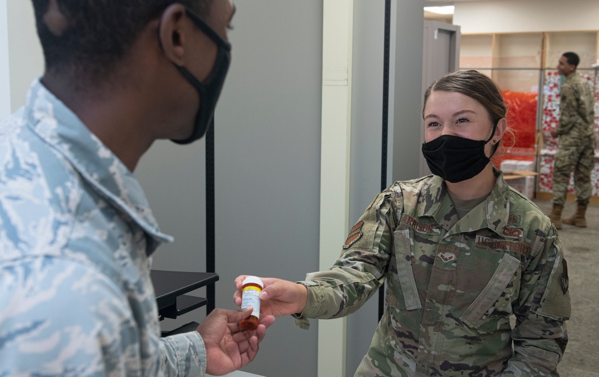 An Airman hands another Airman a prescription bottle