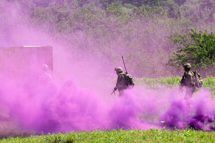 Soldiers move through a plume of purple smoke.