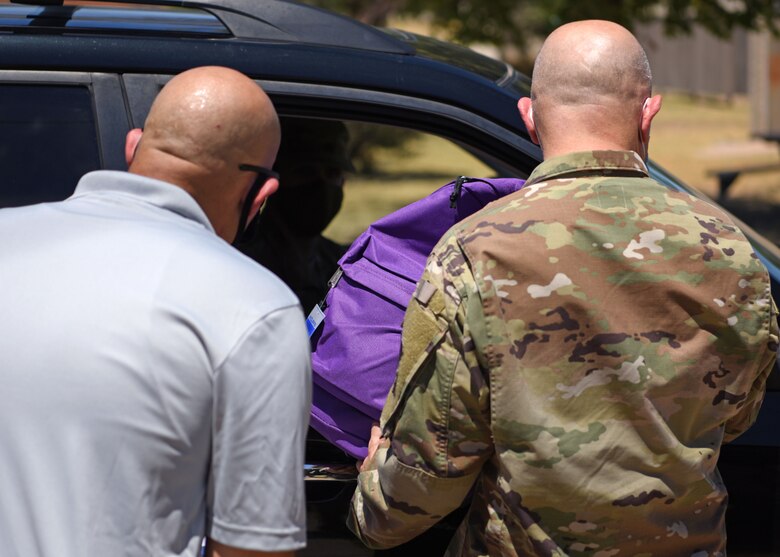 U.S. Air Force Master Sgt. Luis Soto, 17th Communications Squadron first sergeant, and Col. Andres Nazario, 17th Training Wing commander, hand a bag full of school supplies to a military member at Goodfellow Air Force Base, Texas, Aug. 14, 2020. Soto led the charge to gather supplies for the bags and traveled to four locations to get all of the supplies. (U.S. Air Force photo by Airman 1st Class Ethan Sherwood)