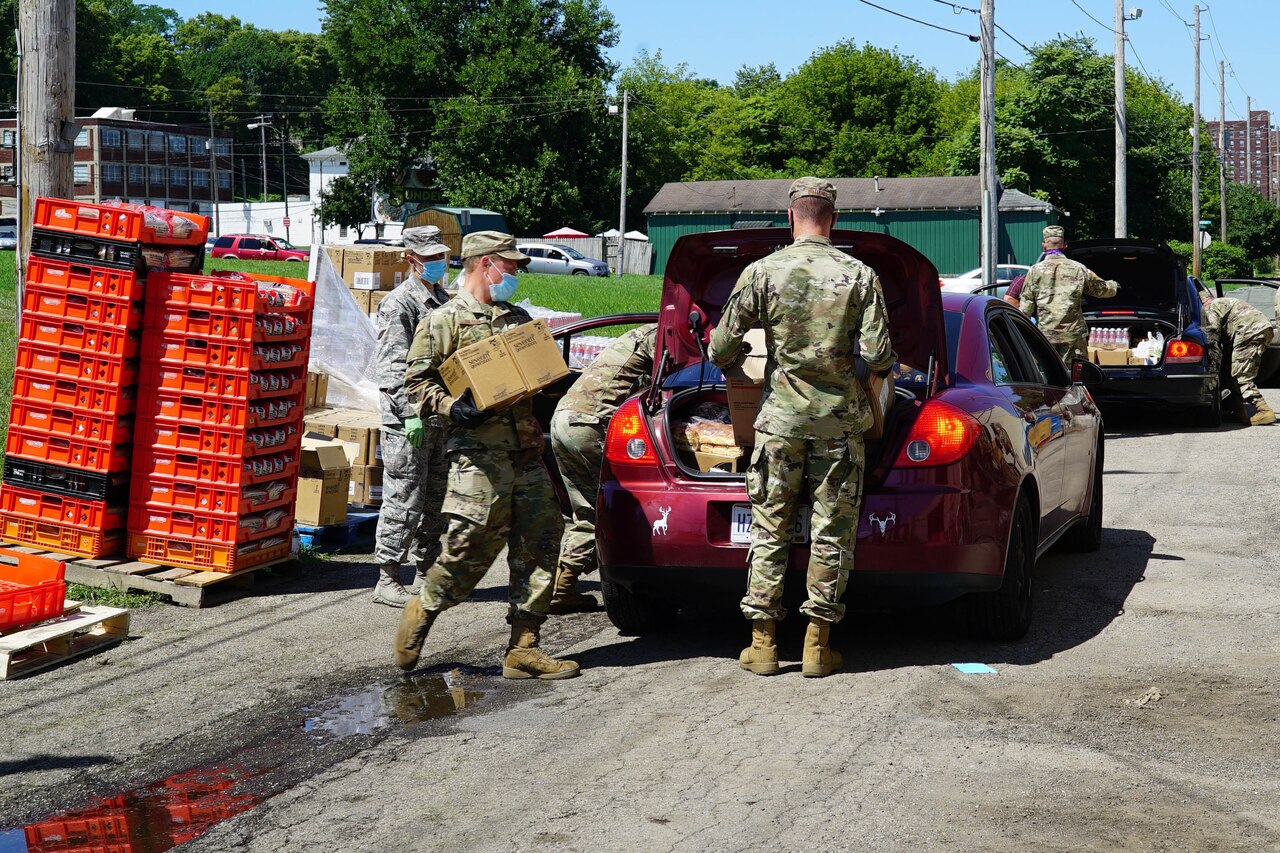 Soldiers wearing face masks load food into waiting vehicles.