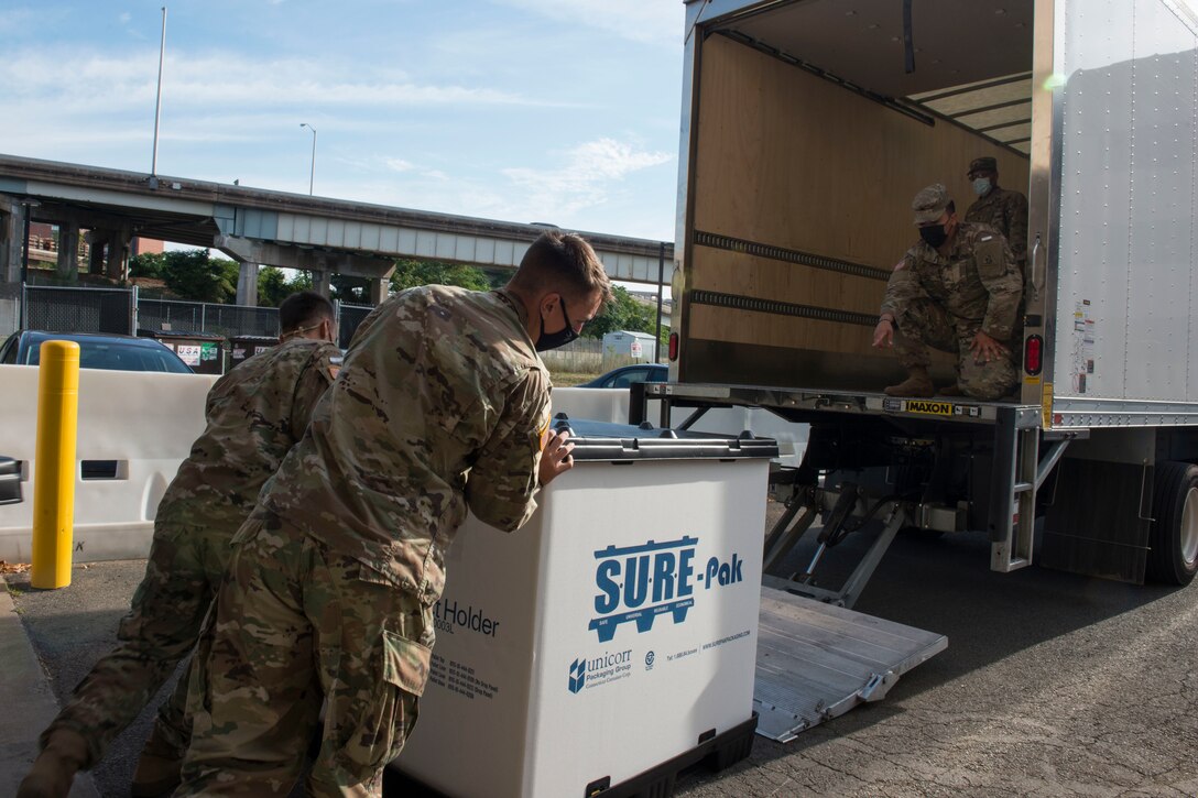 Soldiers load a large container of supplies onto a truck.