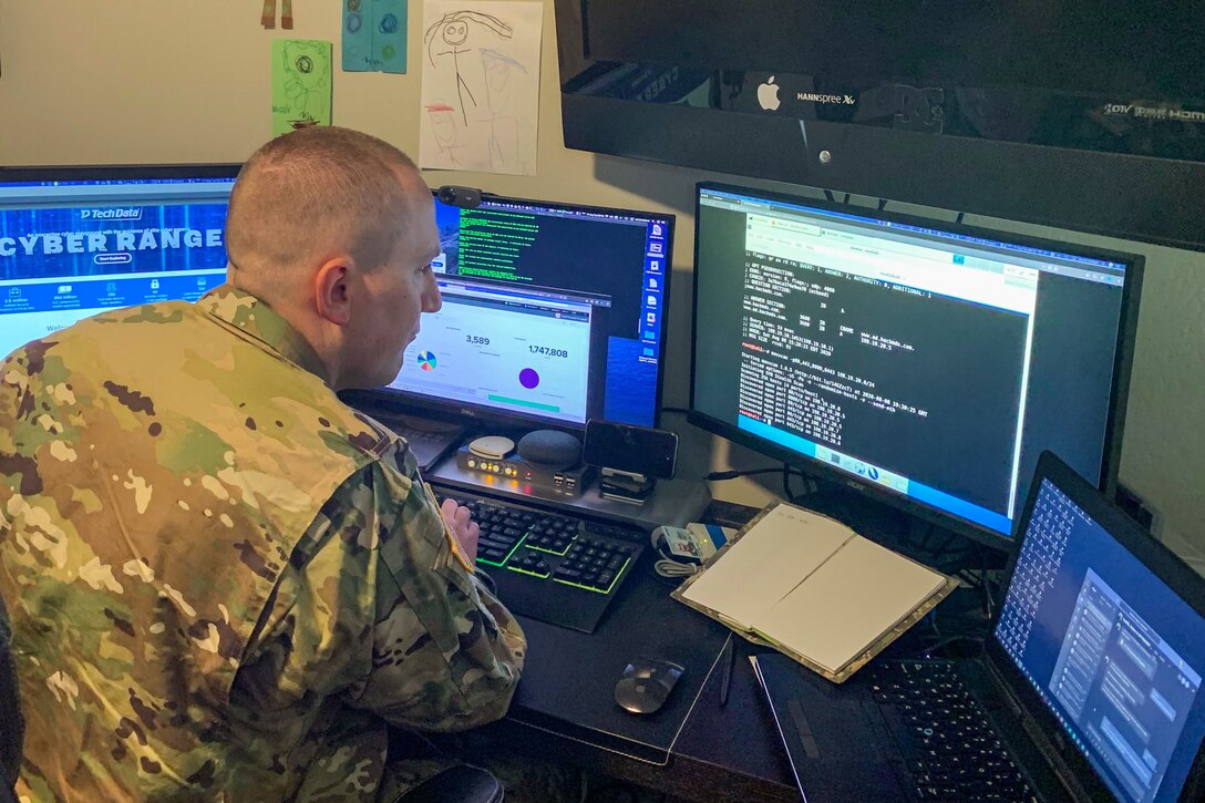 A soldier works at a computer station with four monitors.