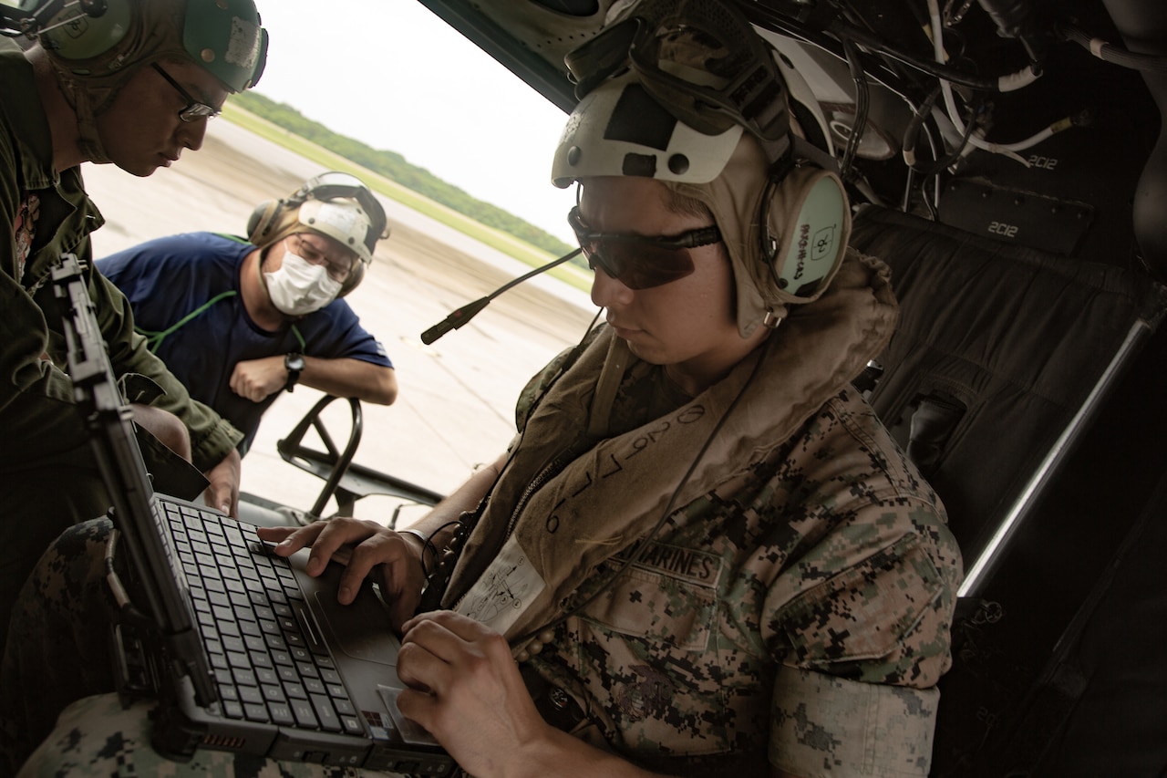 A Marine seated in a helicopter works on a laptop computer.