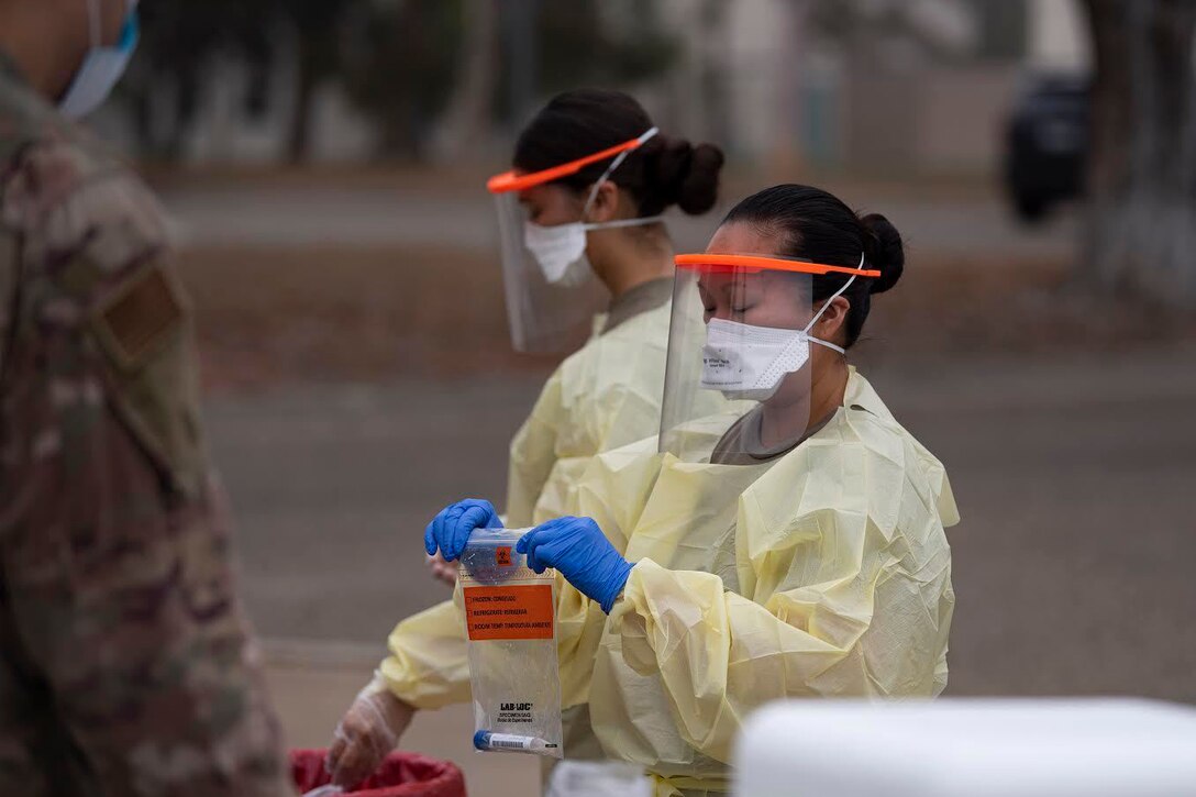 A woman wearing a medical outfit and a mask seals a plastic bag.