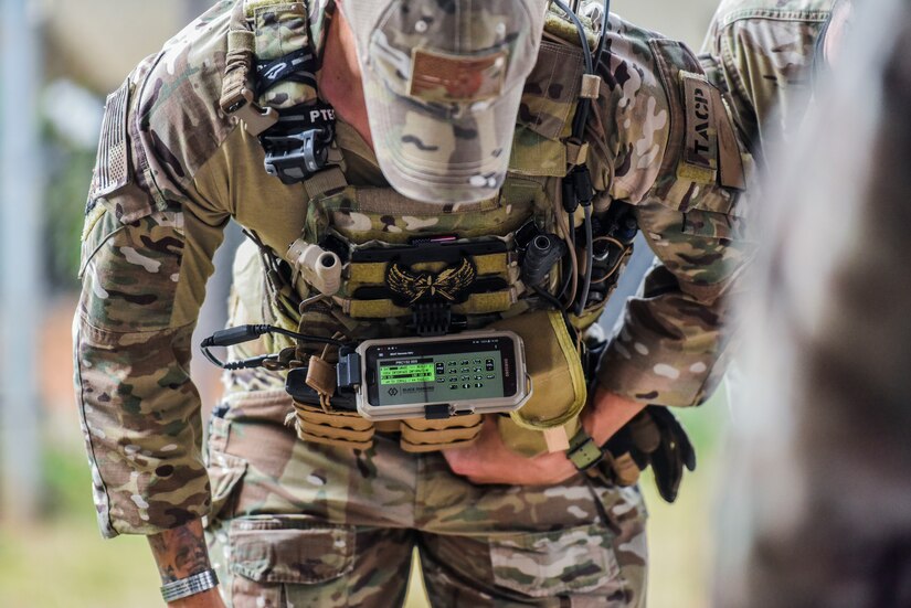 An airman works on a smartphone mounted to his body armor.