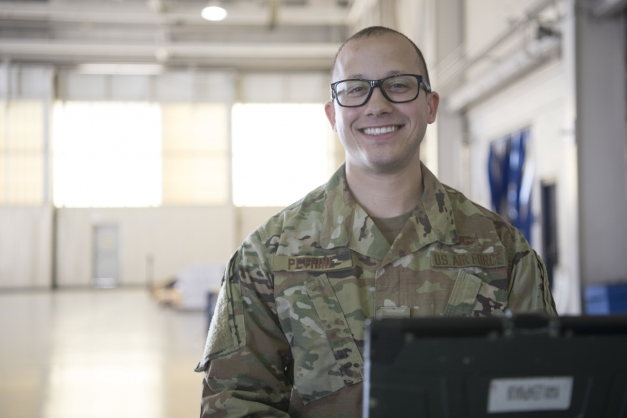 An Airman smiles at the camera inside of an aircraft hangar