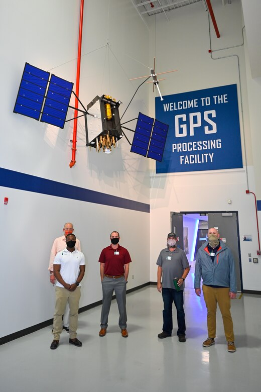 Airmen gather near a GPS III model at Lockheed Martin prior to entering a restricted area Aug. 6, 2020, in Littleton, Colorado. During the tour, Airmen learned about the care Lockheed Martin employees put into building satellites. During the core mate process, workers use a two-ton crane to rotate and lower a satellite into the vertical propulsion core while crew members ensure systems and equipment are intact. (Courtesy photo)