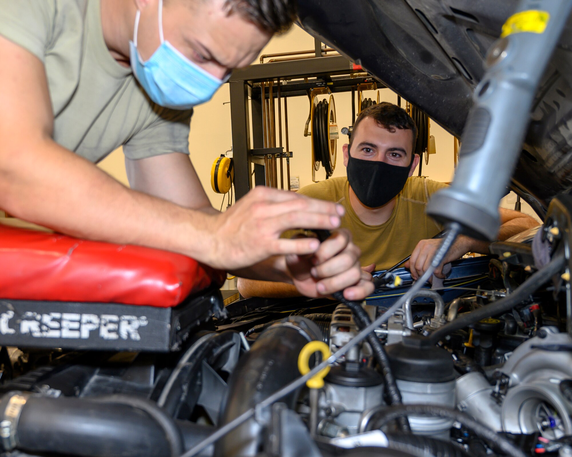 Two Airmen conduct routine vehicle maintenance in a engine bay of a vehicle.