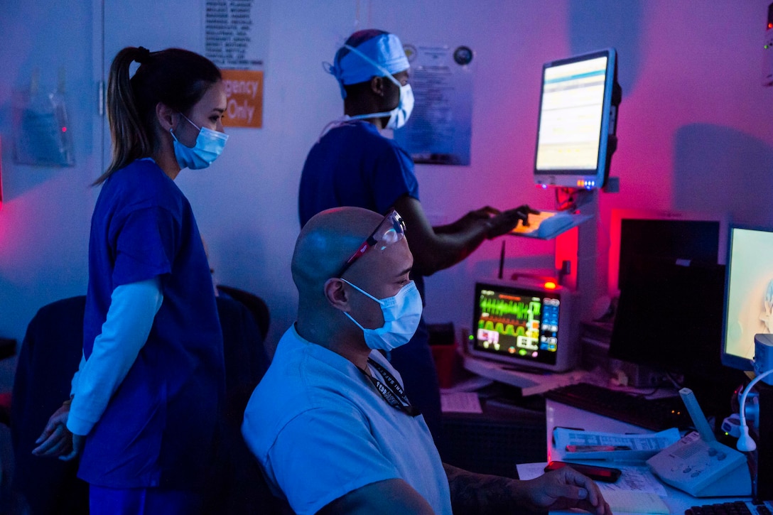 Three people stand in a darkened room looking at monitors.