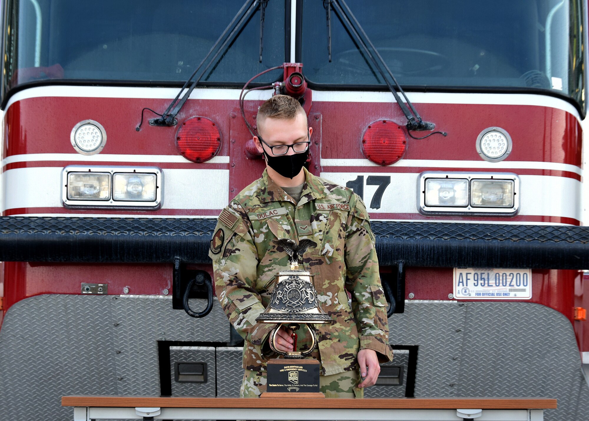 photo of a U.S. Air Force Airman in front of a fire truck ringing a bell