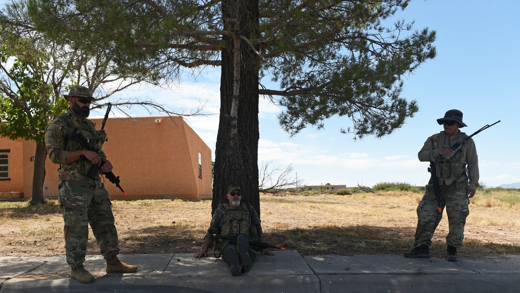 photo of three people, simulating enemy forces, waiting under the shade of a tree