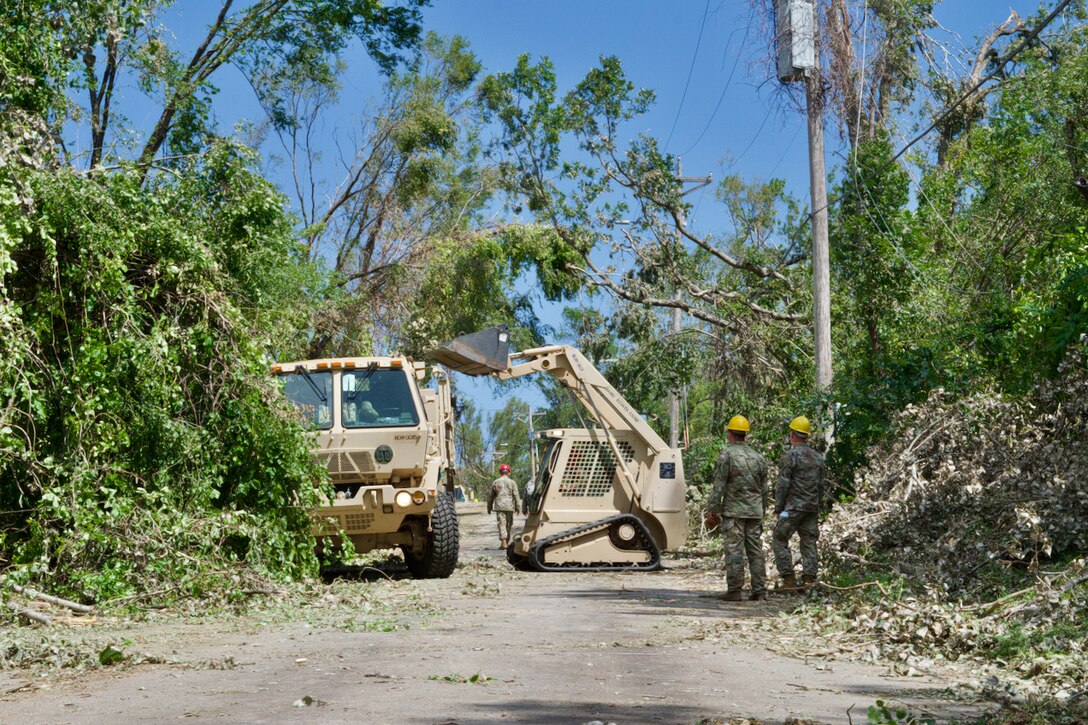 Soldiers watch a small bulldozer dump debris into a truck.