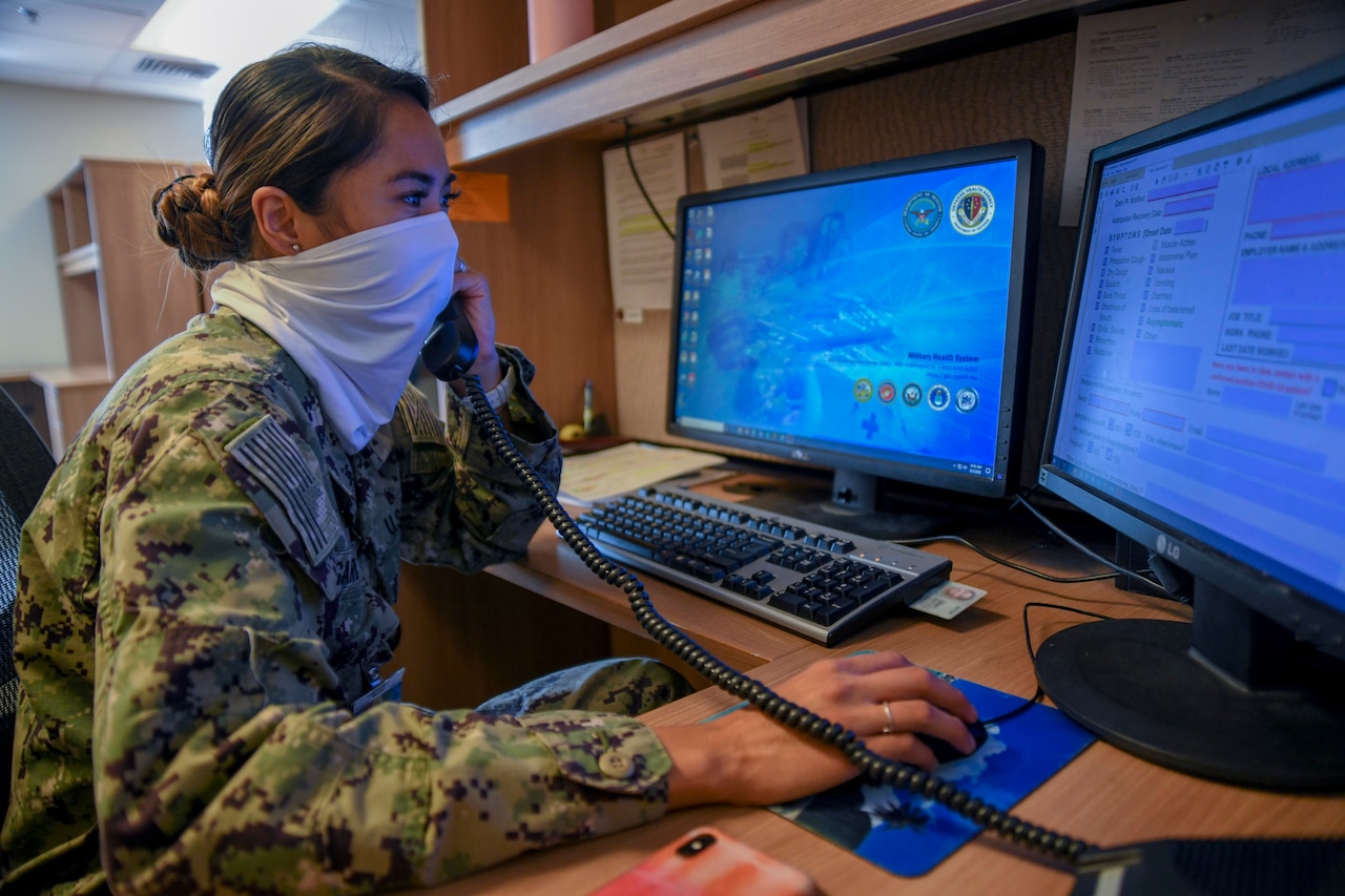 A sailor wearing a face mask talks on a phone.