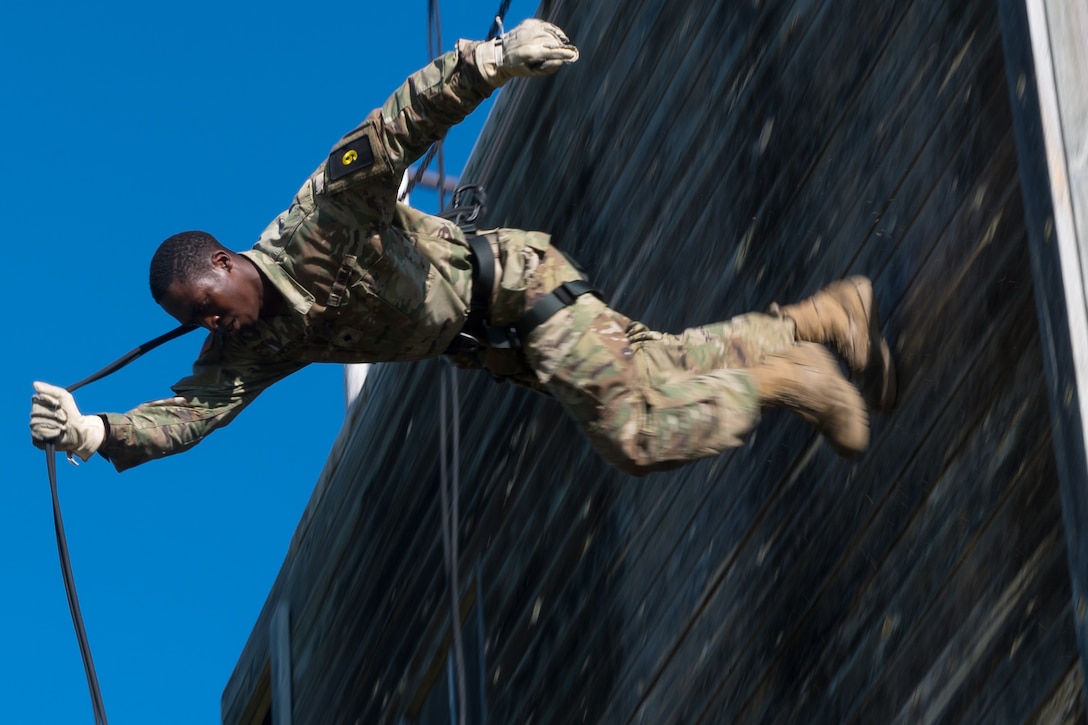 A soldier uses a rope to rappel down a wall.
