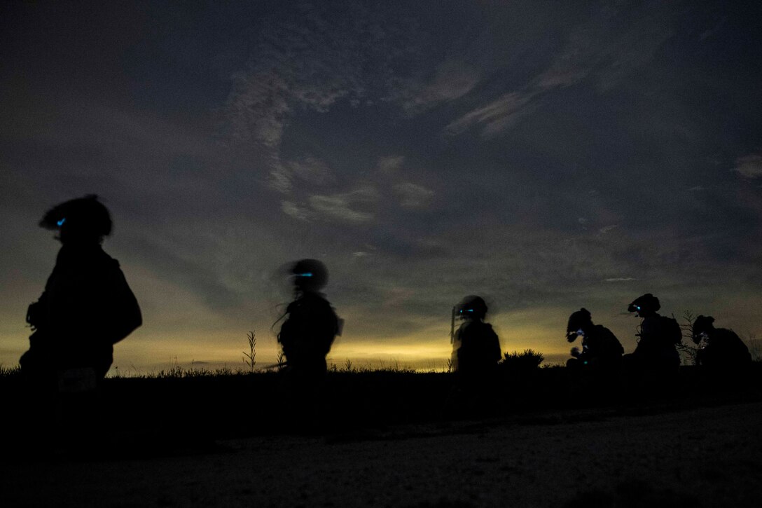 Service members walk in a row at night.