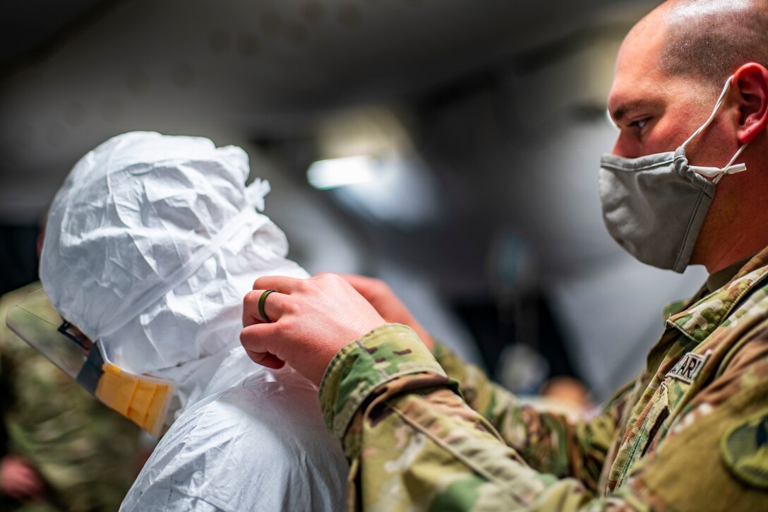 A soldier wearing a face mask helps another soldier put on his medical protective suit