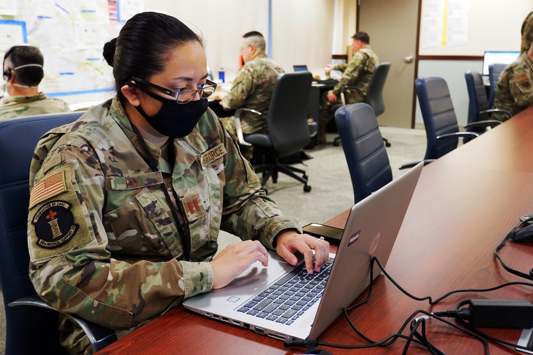 An Air Force officer wearing a face mask works at a laptop computer.