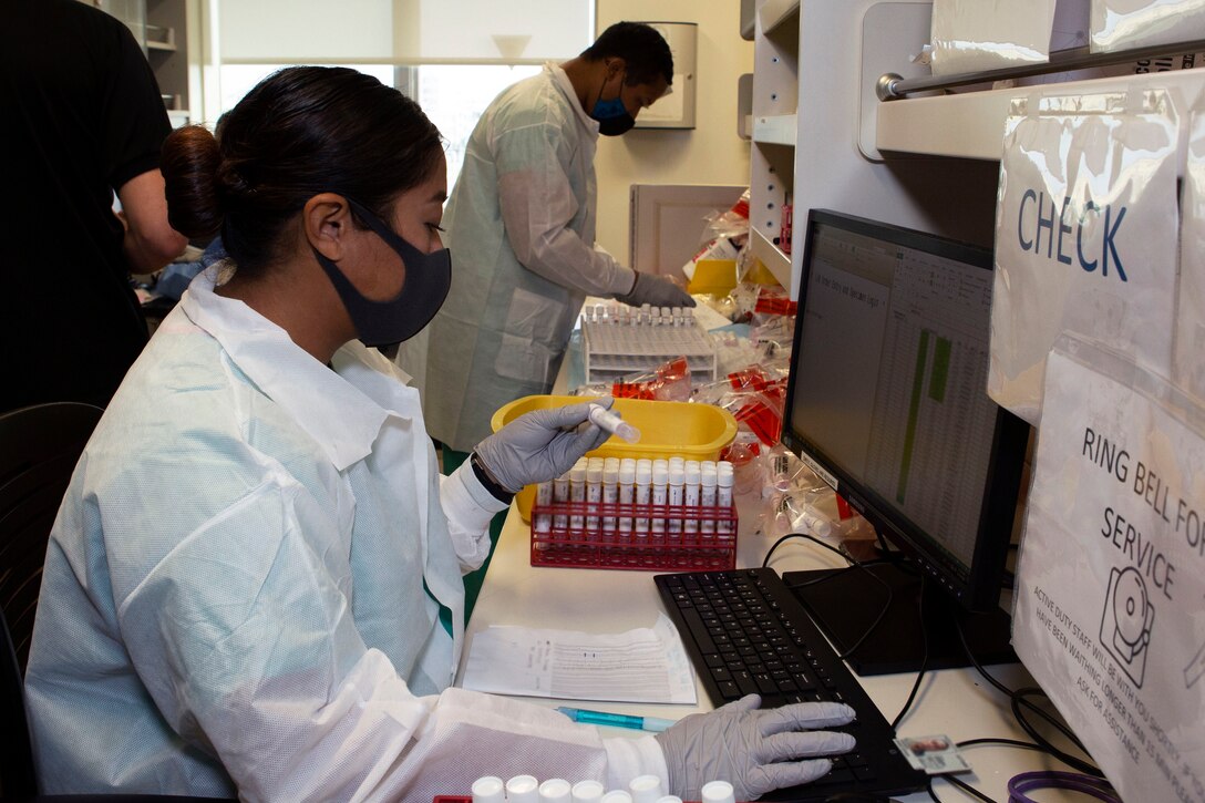 A sailor wearing personal protective equipment takes inventory of COVID-19 test samples