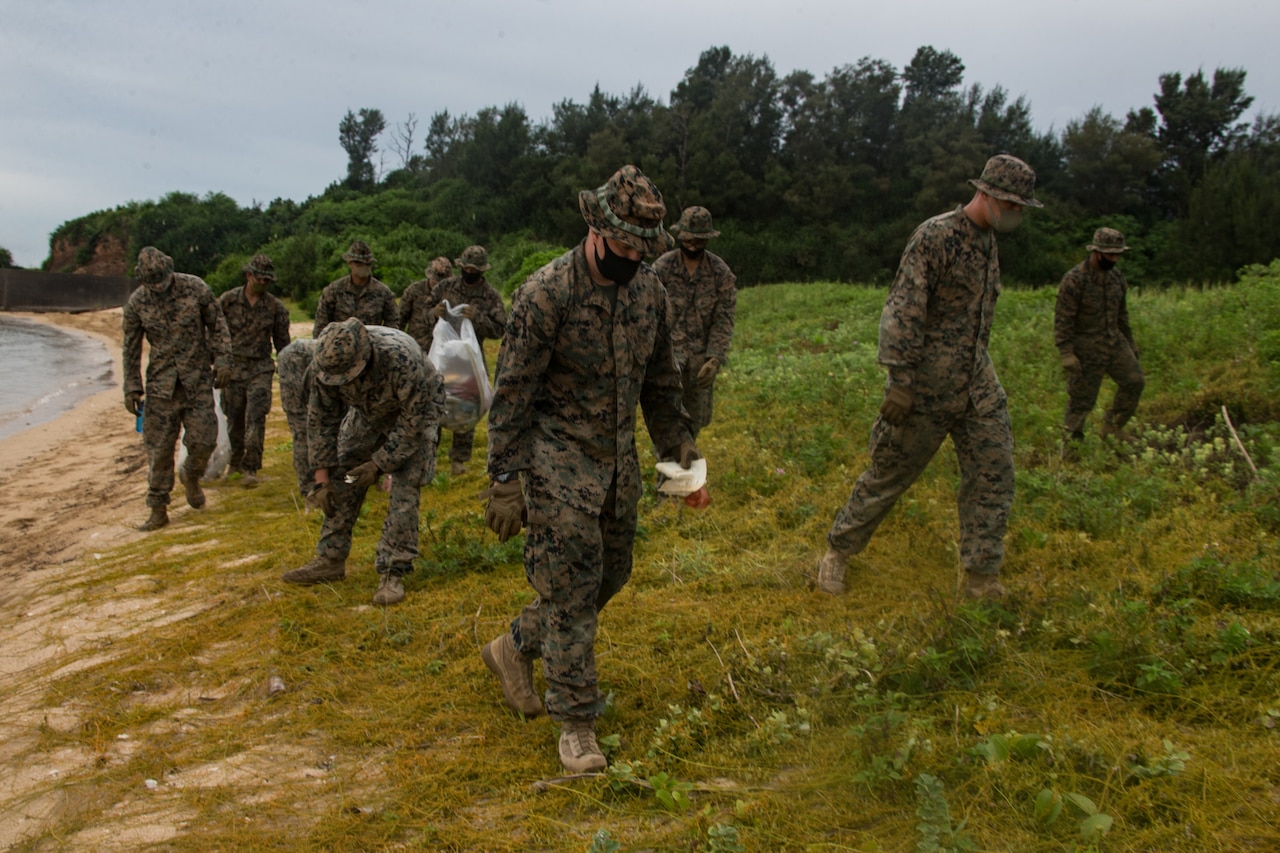 Marines pick up trash on a beach.