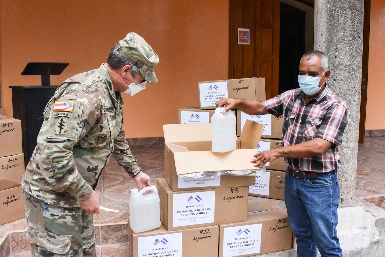 A soldier and a civilian, both wearing face masks, unpack boxes of medical supplies.