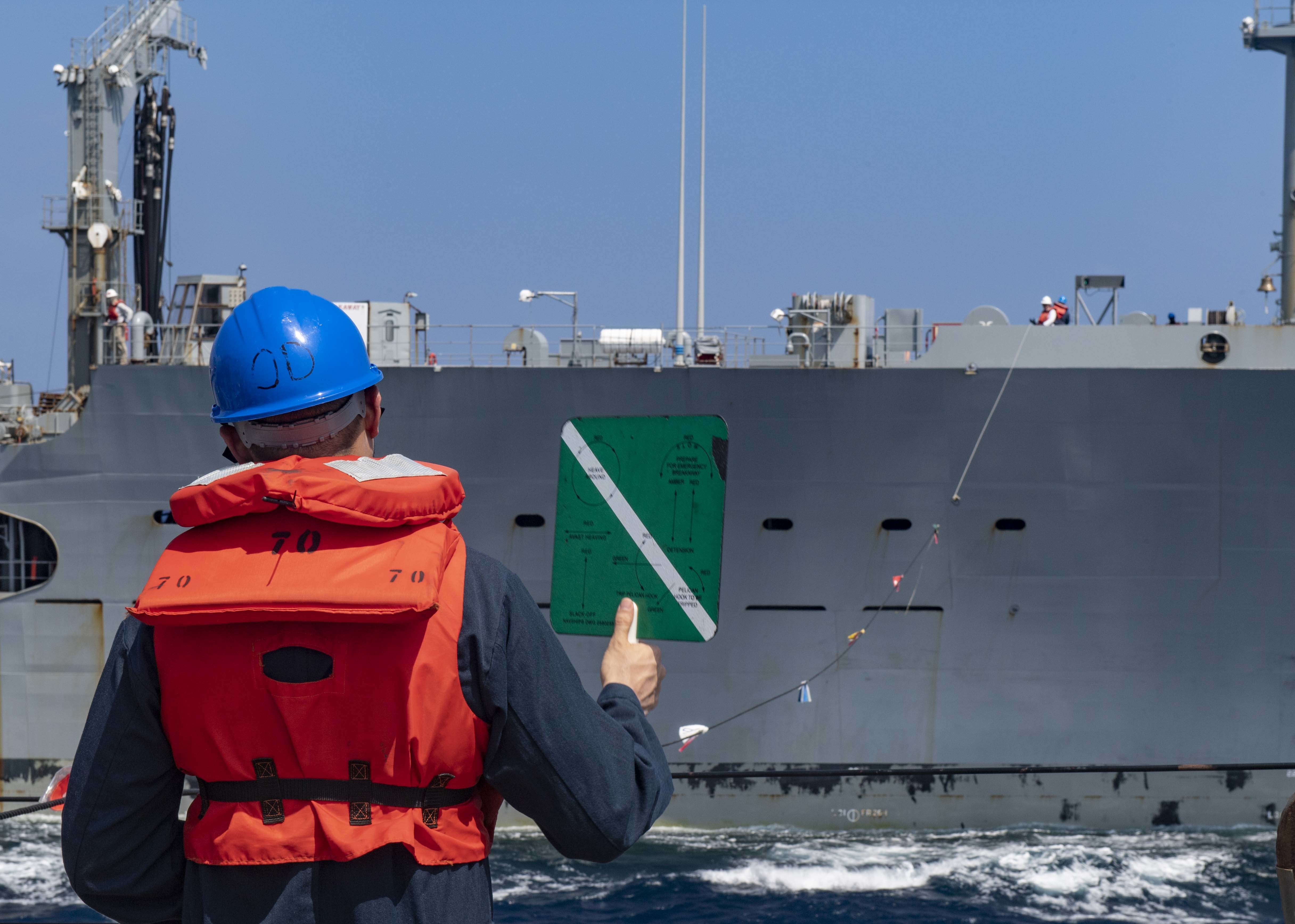 Personnel Specialist 2nd Class Michael Revron, assigned to USS Mustin (DDG 89), signals  to the USNS John Ericsson (T-AO 194) during a replenishment-at-sea.