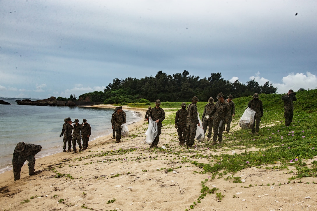 A group of Marines walk on a beach picking up trash.