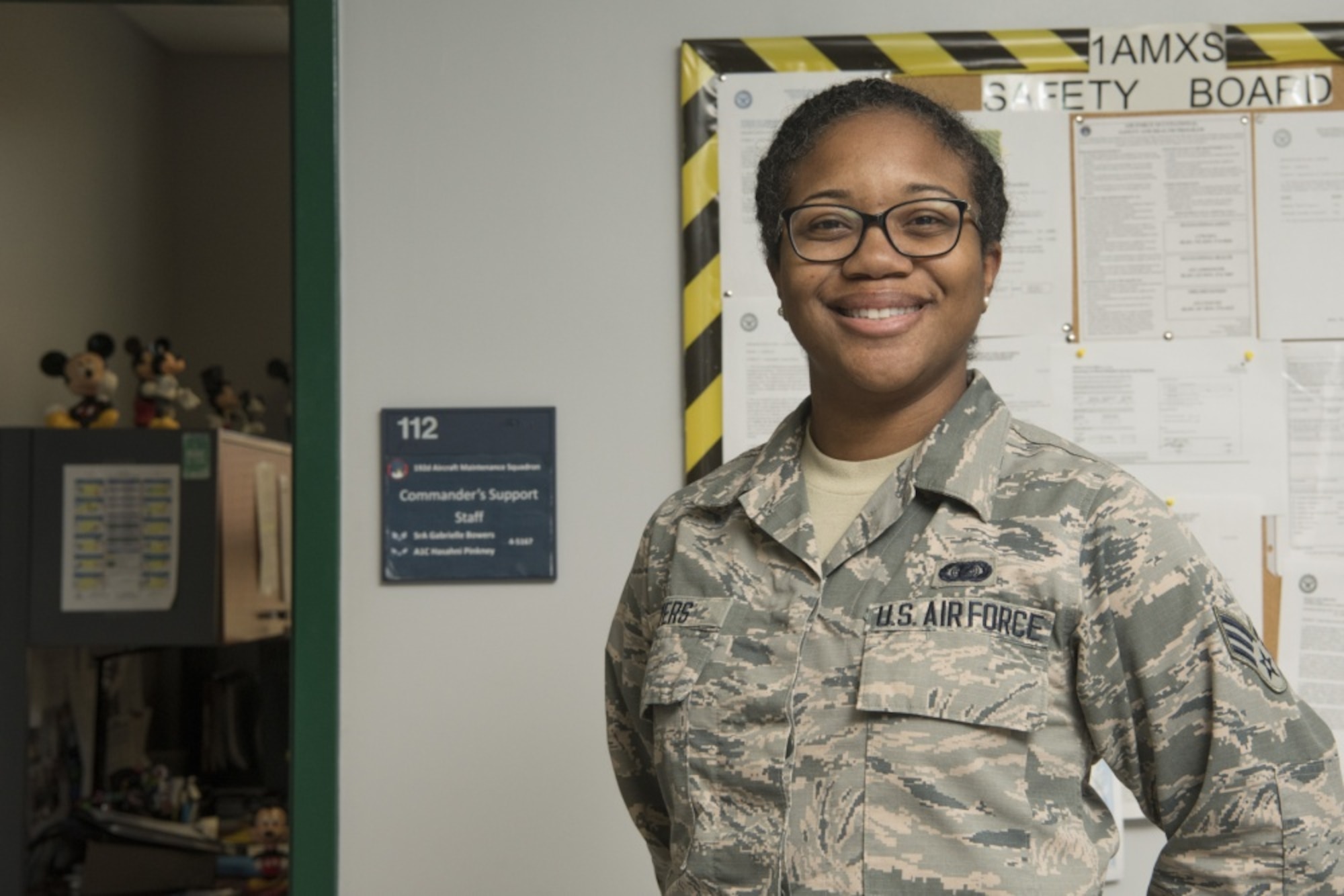 A female Airman smiles at the camera standing outside of her office