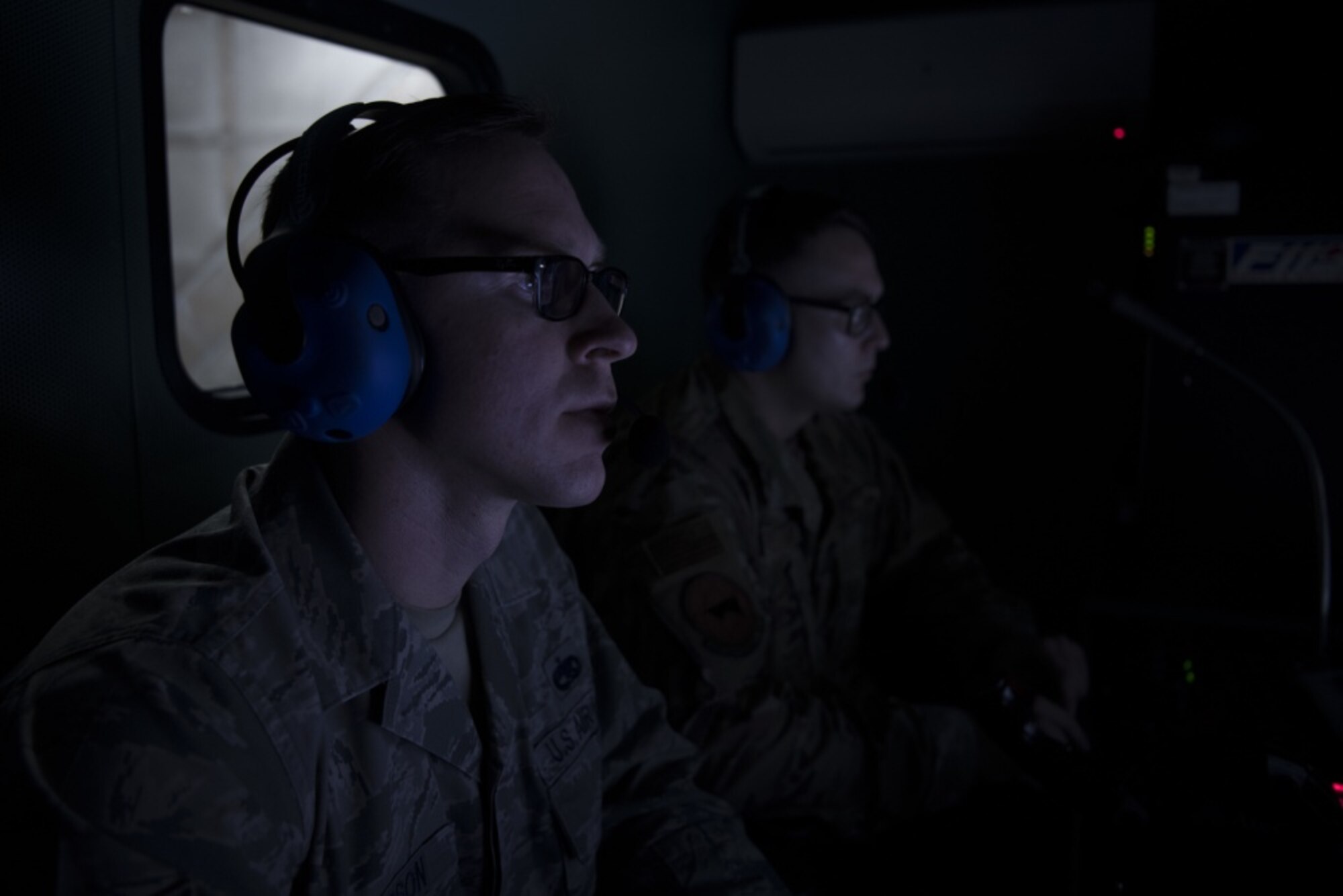 Two Airmen watch computer screens in a dark room
