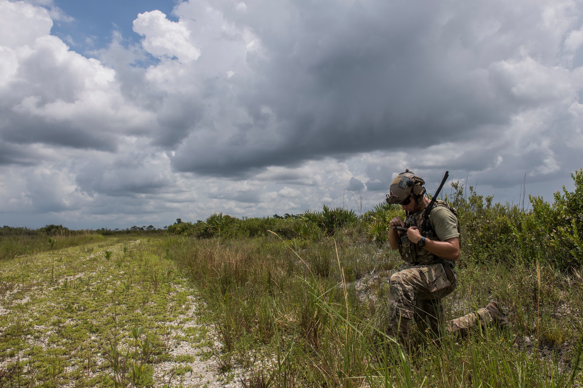 A special operations operator kneels in high grass while talking into his radio gear as part of close air support training during the Special Operations Terminal Attack Controller Course at Avon Park Florida, Aug. 6, 2020