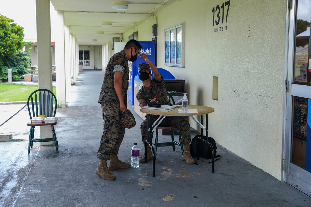 A Marine wearing a face mask takes the temperature of another Marine wearing a face mask.