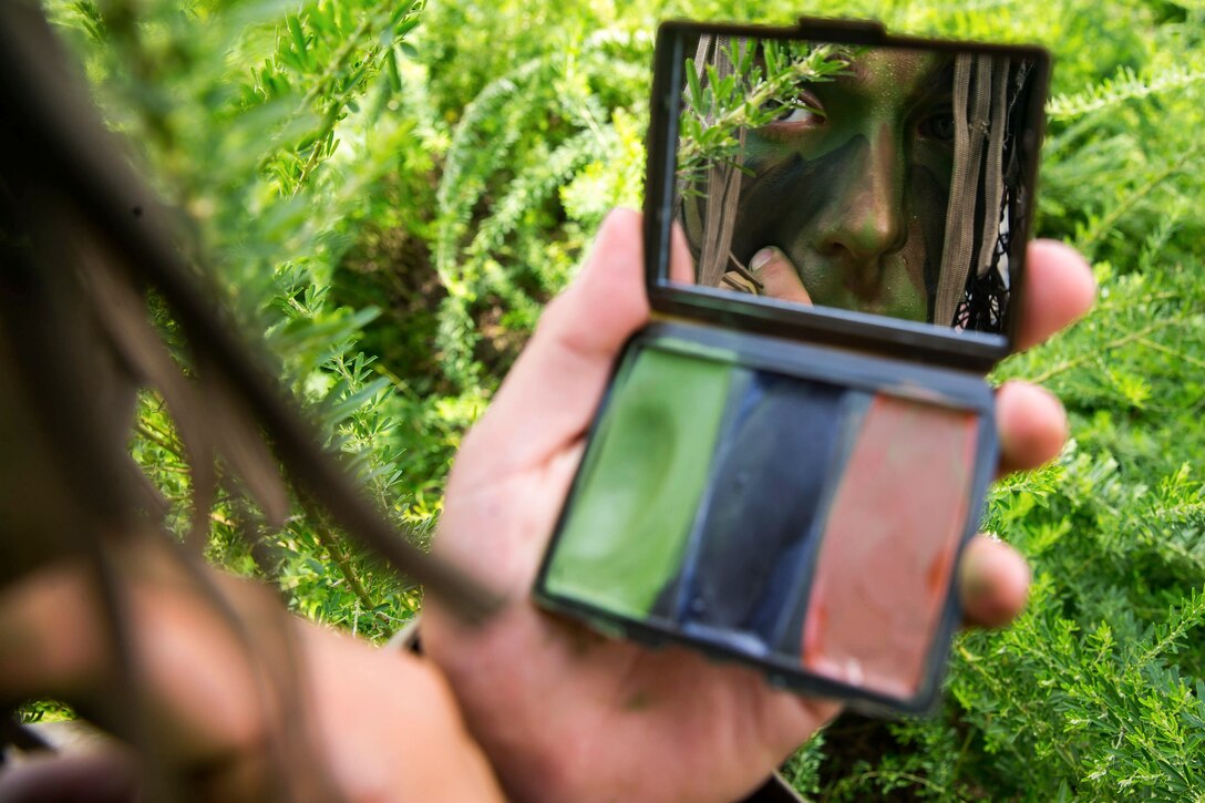 A Marine looks at himself in the mirror of a camouflage paint compact.