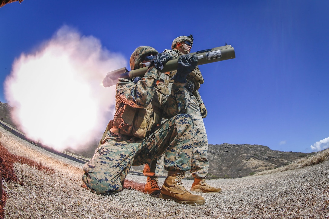 A Marine fires a weapon as another Marine watches.
