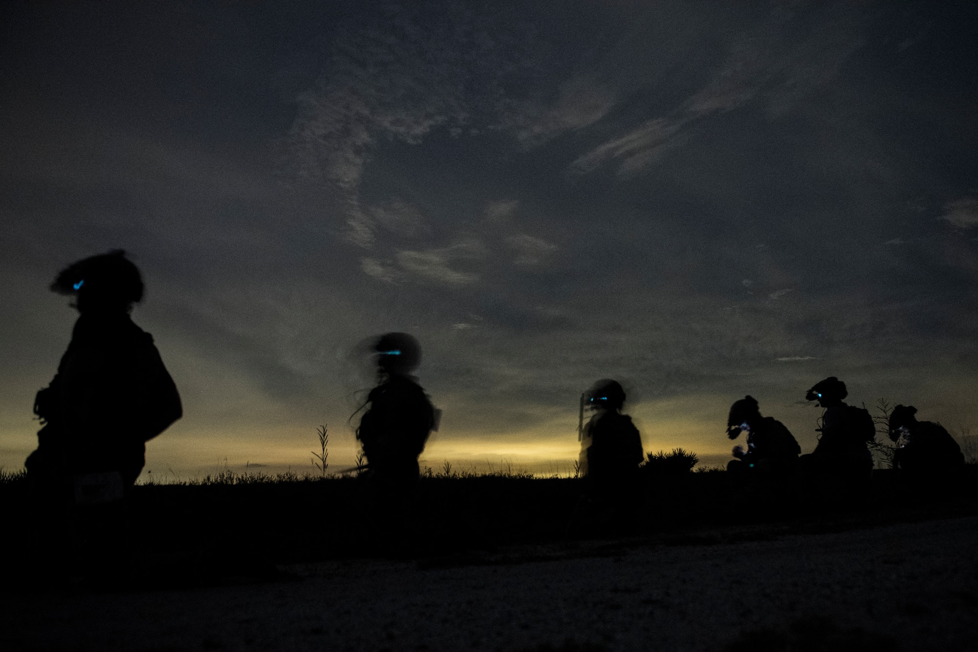A half dozen special operations troops stand spaced apart in a line profiled by a narrow streak of sunset in the background. Special operations troops from the Army, Air Force and Marine Corps conducted close air support during the Special Operations Terminal Attack Controller Course at Avon Park Florida, Aug. 6, 2020.
