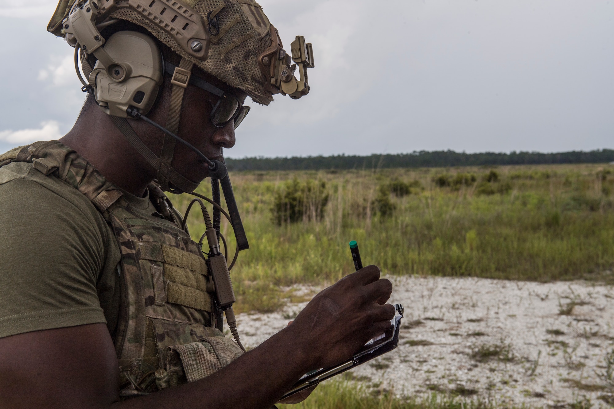 A special operations troop uses a stylus to update his handheld tablet device with sand and tall grass in the background.