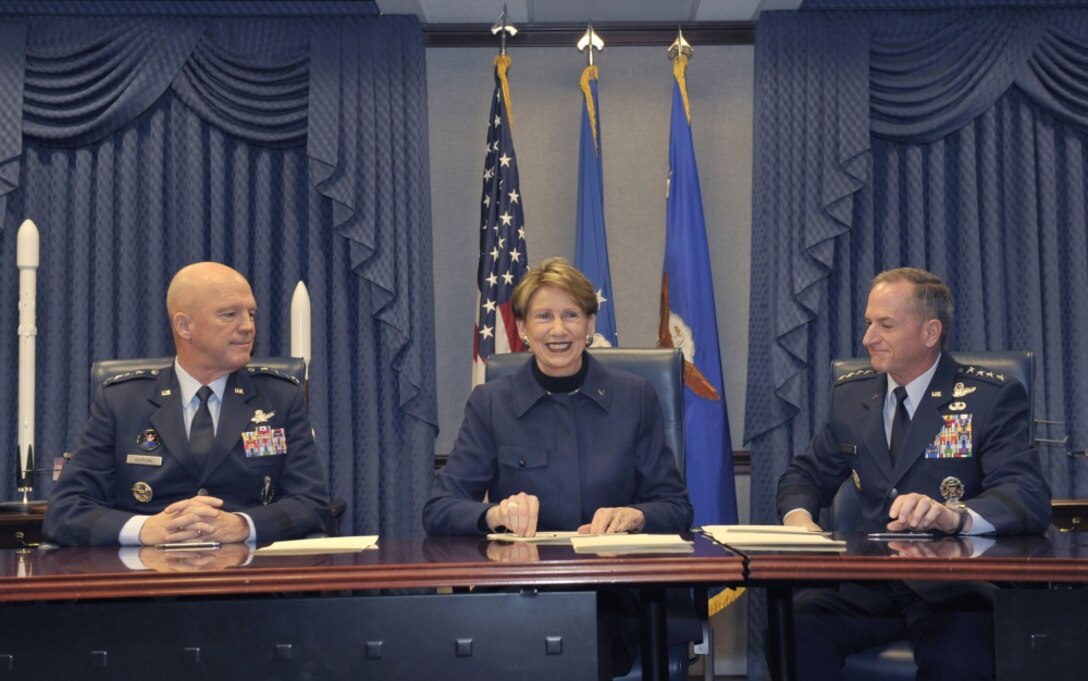 A civilian woman sits between two Air Force generals after signing official documents.